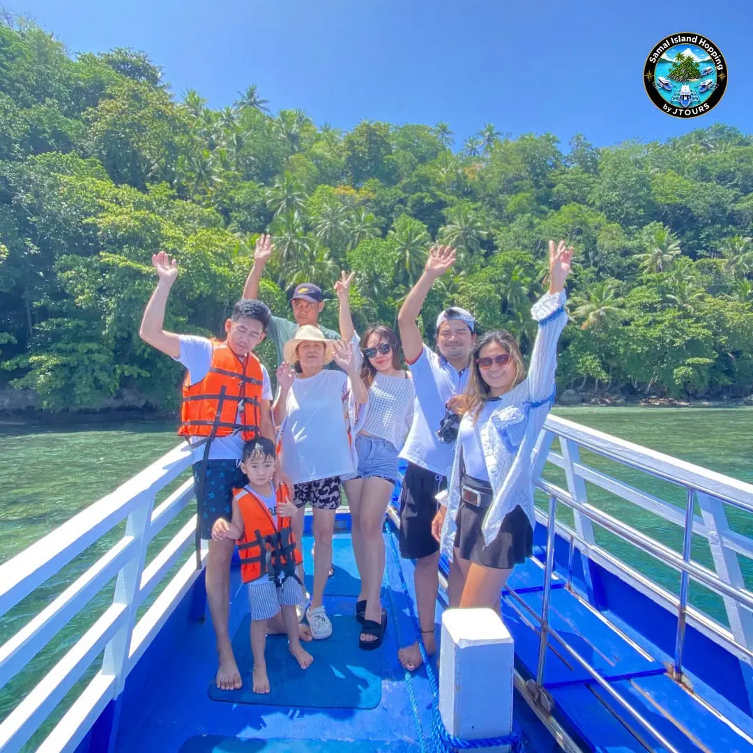 Guests in life vests waving from the boat deck near a green island