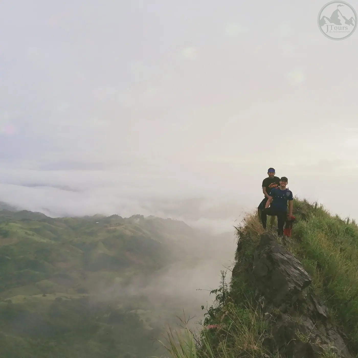 Two hikers resting on a misty ridge above the clouds